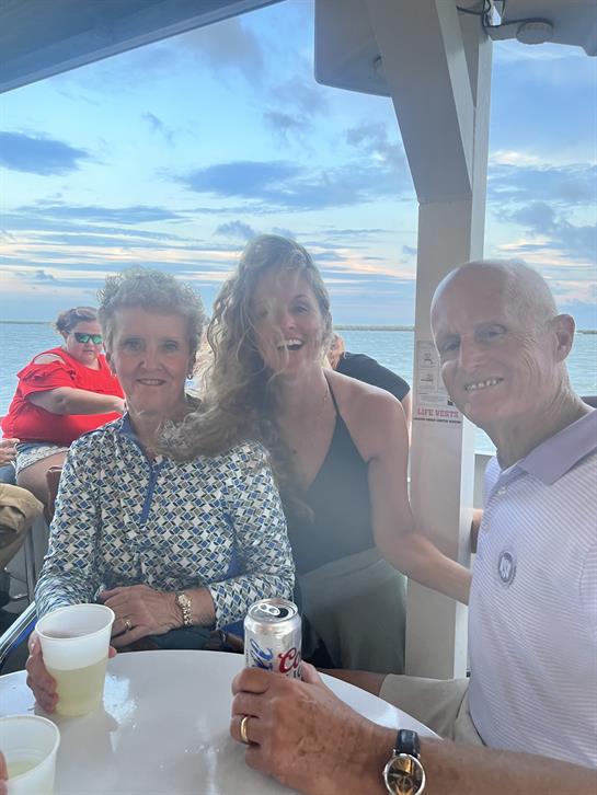 Group of friends sharing smiles and drinks while relaxing by the water during sunset.