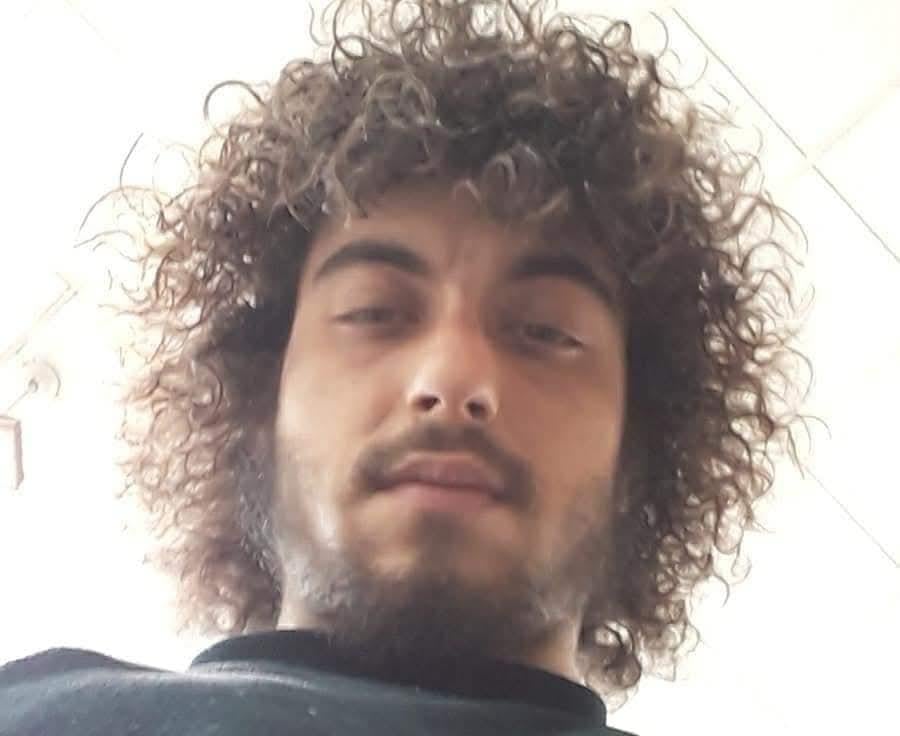 A young man with curly hair poses and looks down into the camera, showing playful expression.