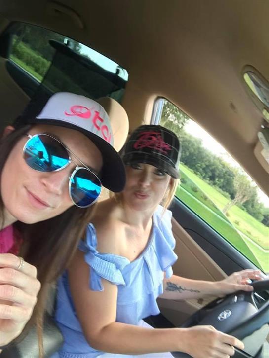 Two friends smile while taking a selfie during a lively drive in a truck on a sunny day.