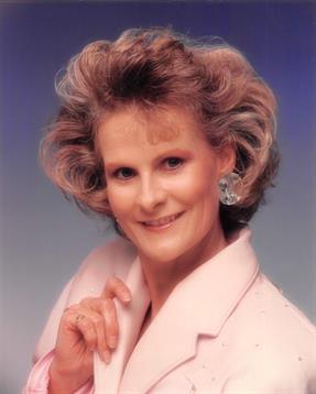 Outside light reflects softly as a woman poses with a warm smile in a studio.