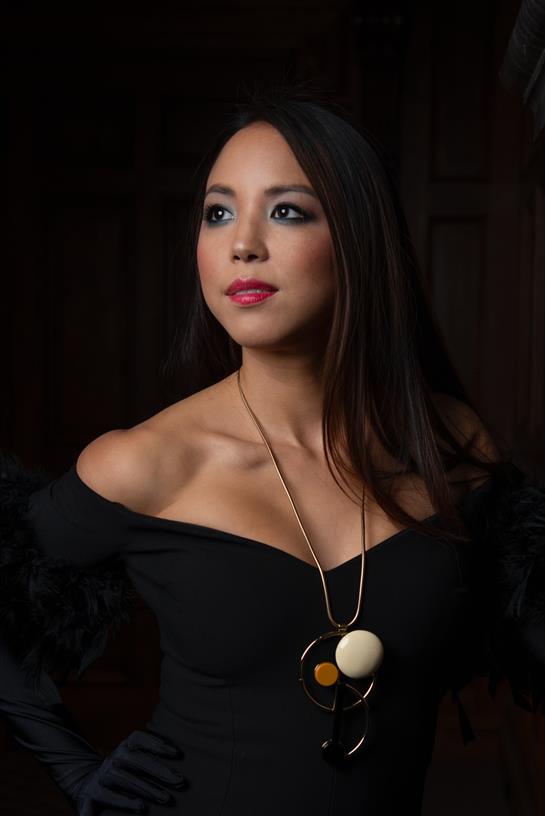 A woman stands in a stylish black off-shoulder outfit showcasing her elegant jewelry.