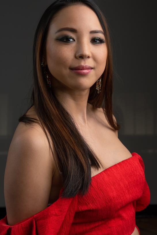 A confident woman models an elegant red strapless dress in a studio.