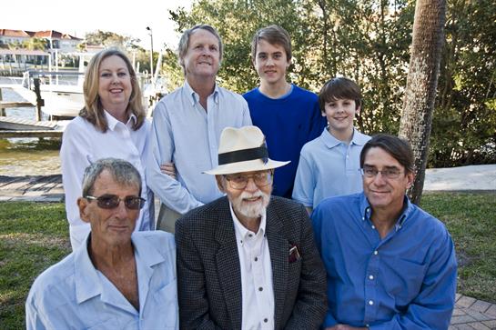 A joyful family gathering occurs in a park with several generations posing together happily.