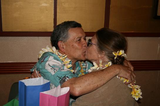 A couple embraces, sharing a tender kiss while wearing floral leis in a joyful atmosphere.