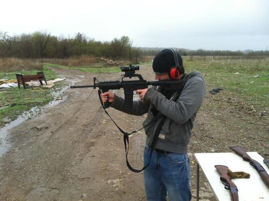 Individual focuses on aiming a firearm while standing at a shooting range in nature.
