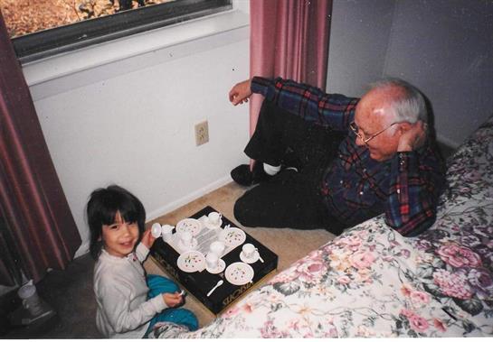 A young girl and her grandfather share a delightful tea party on the floor, surrounded by cups.