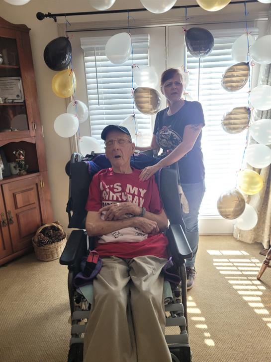 A man in a wheelchair is enjoying a celebration while a woman stands behind him, smiling.