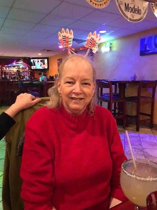 A cheerful woman in a red sweater sits at a bar, wearing festive antler headband decorations.