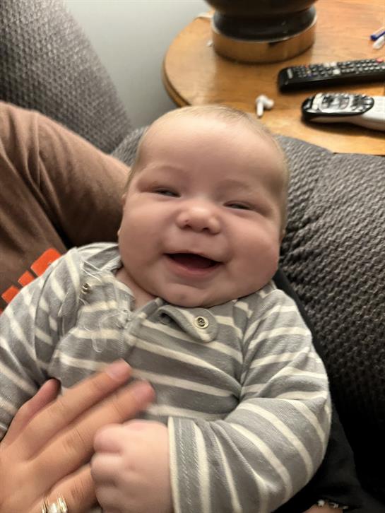A joyful baby with a big smile enjoys a cuddly moment being held in a soft gray couch.