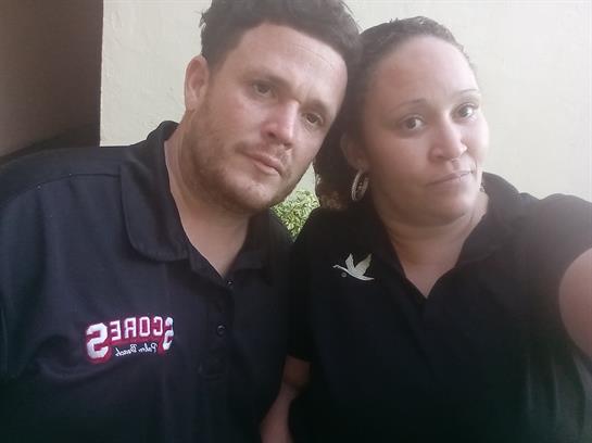 Two friends stand together in a casual outdoor setting, smiling and enjoying their time.