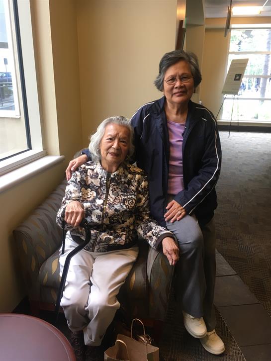 Two women sit comfortably on a couch, enjoying each other's company in a warm indoor space.