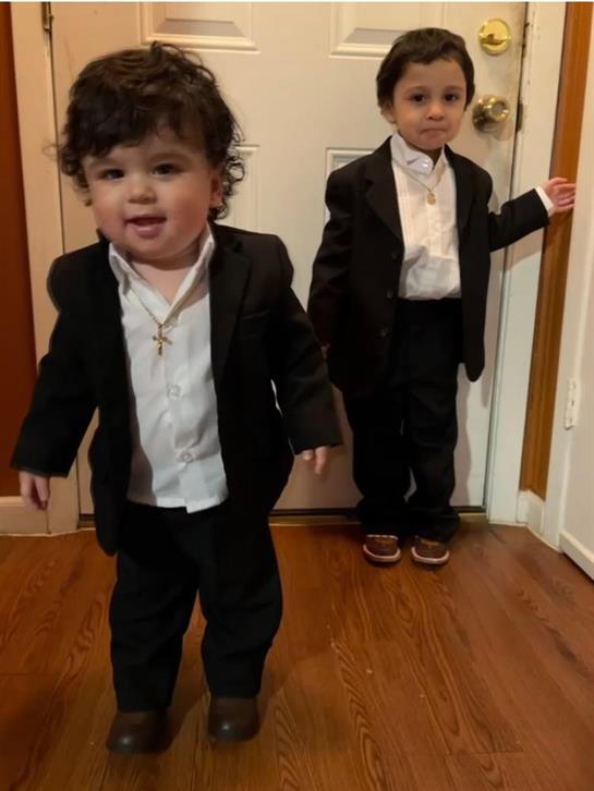 Two boys in formal suits playfully pose at home, expressing happiness and excitement.