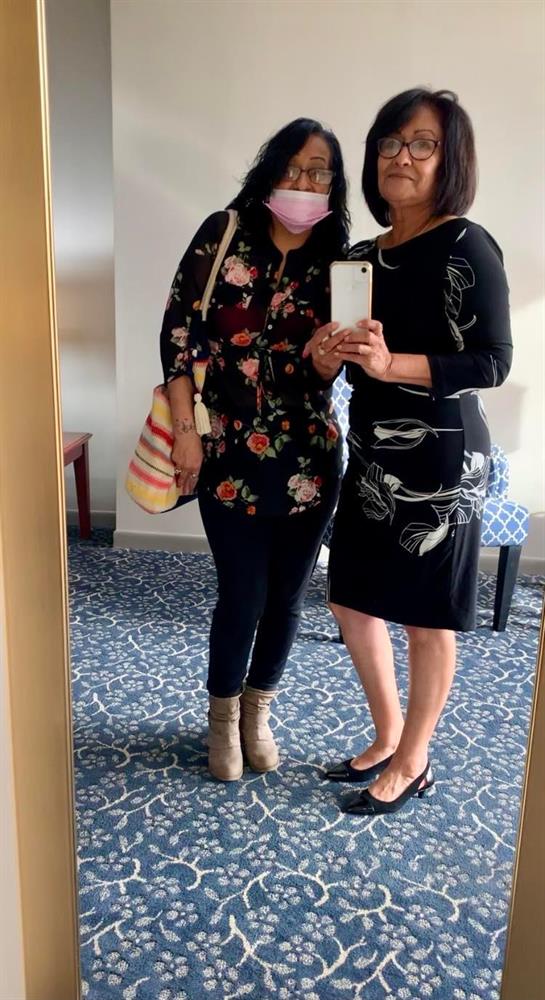 Two women smile for a selfie in a hotel lobby while showcasing their fashionable outfits.