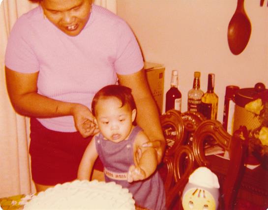 Family member assists child at a festive birthday gathering with a cake and joyful atmosphere.