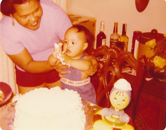 A smiling father holds a toddler near a beautifully decorated birthday cake while celebrating.