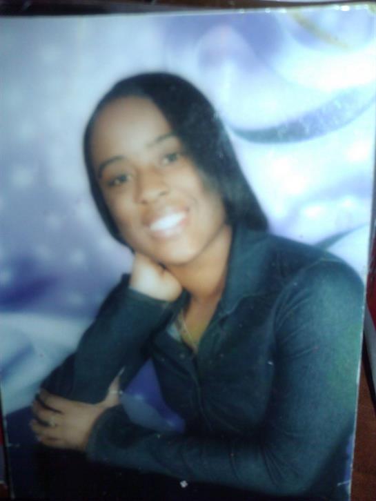 A young woman poses with a smile, her long hair styled elegantly, while dressed in a black outfit.