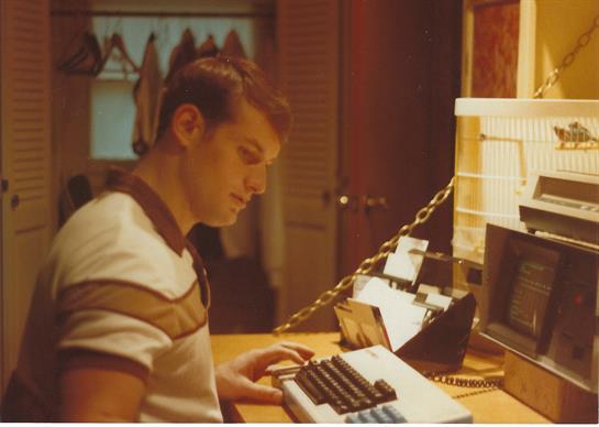 A young man focuses intently on typing at a retro typewriter in a warmly lit room.