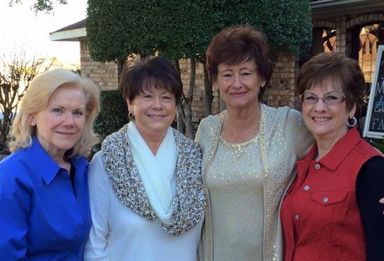 Four women stand together in a garden, smiling happily while posing for a picture during daylight.