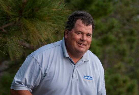 A man dressed in casual attire enjoys a moment outdoors surrounded by greenery.
