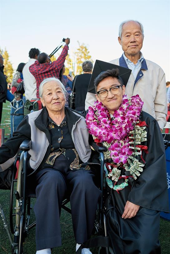 A young graduate in a wheelchair smiles alongside an elder at a graduation event.