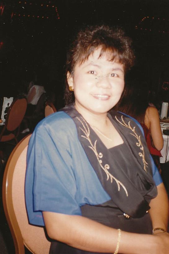 A woman with dark hair and a blue outfit smiles while seated at a lively banquet setting.