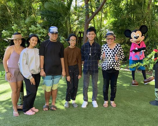 Friends gather in a vibrant garden to celebrate alongside a cheerful animated character.