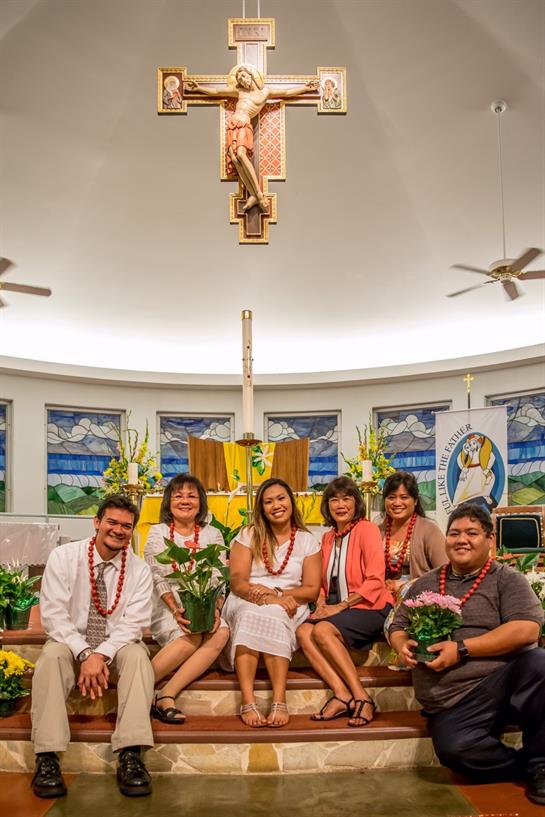 A group of community members gathers in church, surrounded by flowers and vibrant decorations.