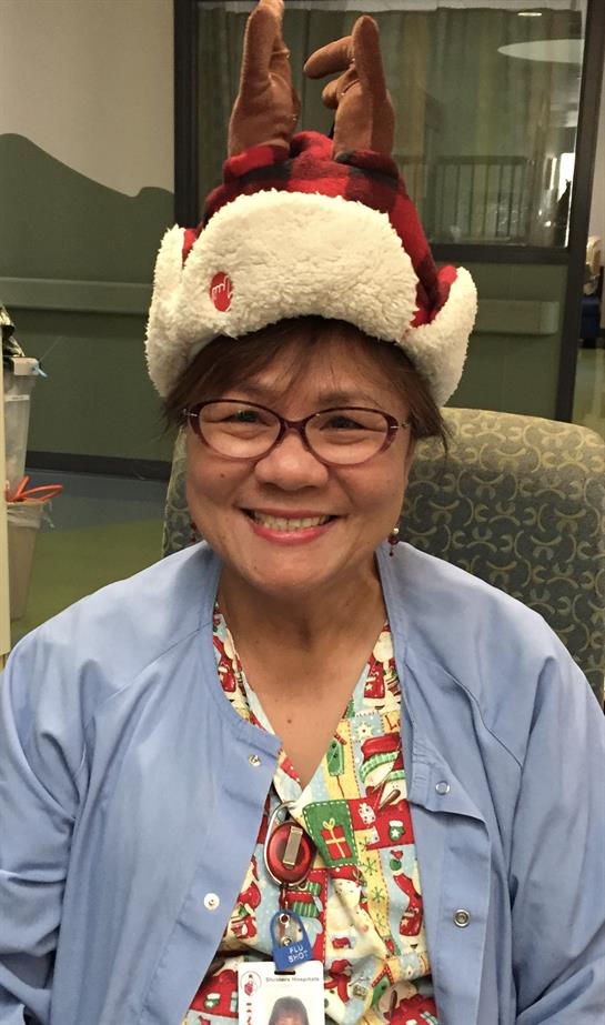 A smiling nurse in scrubs wears a cozy holiday hat, spreading cheer at a healthcare facility.