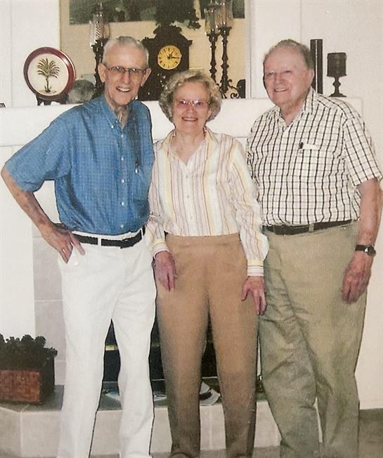 Three seniors stand smiling in a comfortable living room, sharing a joyful moment together.