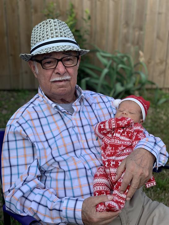 An elderly man sits outside with a baby in his arms, both enjoying a sunny day together.