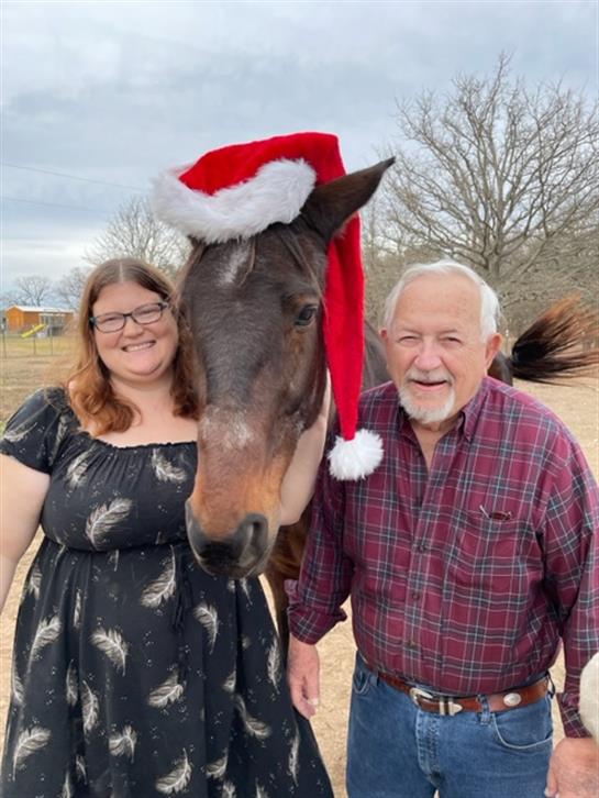 A joyful family moment with a woman and a man beside a horse dressed in a festive Santa hat.