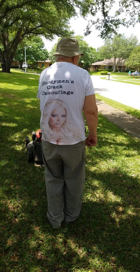 A man mows grass in a residential area, showcasing a funny shirt design that draws attention.