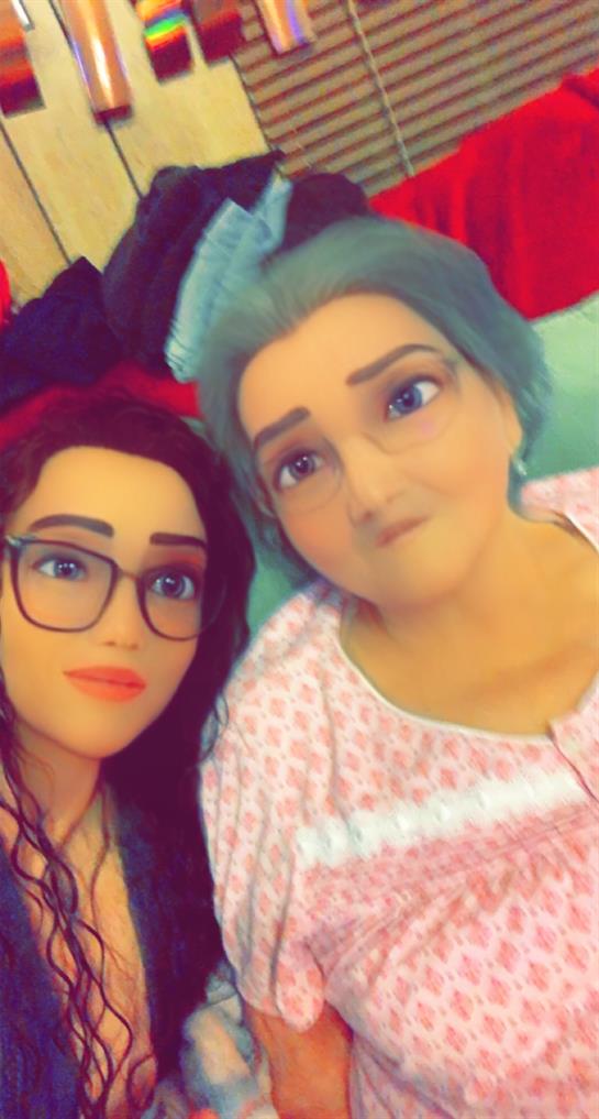 A young woman smiles with a doll that looks like an elderly person in a cozy home setting.