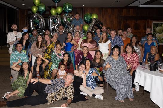 A diverse group of people poses joyfully at a festive celebration with vibrant decorations.