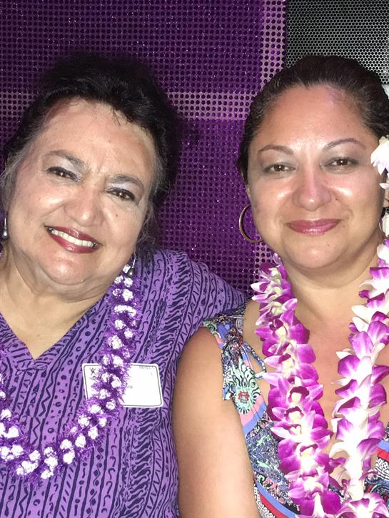 Two women pose happily while adorned with colorful Hawaiian leis at a vibrant celebration.