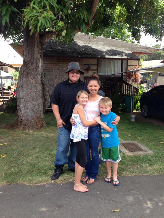 A joyful family stands outside their home, smiling and embracing each other in the garden.