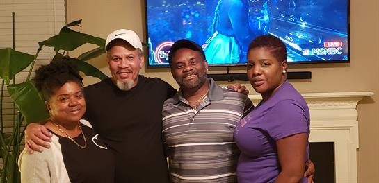 Friends gather in a cozy living room, smiling and celebrating with entertainment on screen.