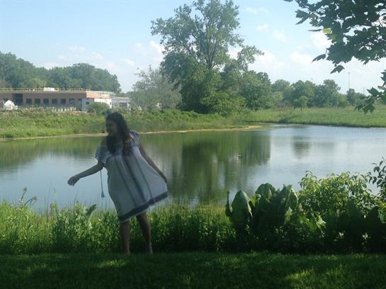 A girl twirls playfully near a serene lake, enjoying the beauty of nature on a sunny day.