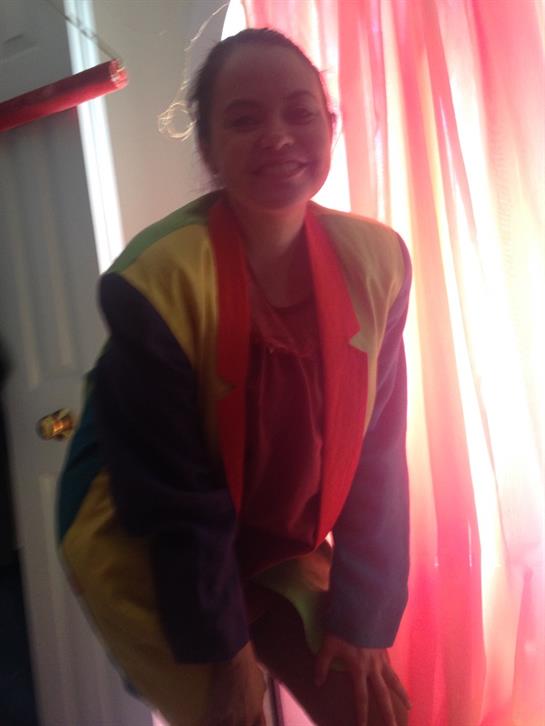 A young person is smiling while wearing a vibrant outfit in a joyful, colorful setting.