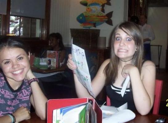 Two friends at a table, one excited with the menu while the other smiles, enjoying dinner.