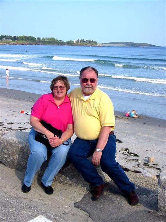 Couple relaxes on a sandy beach while waves crash gently nearby, enjoying a sunny day outdoors.