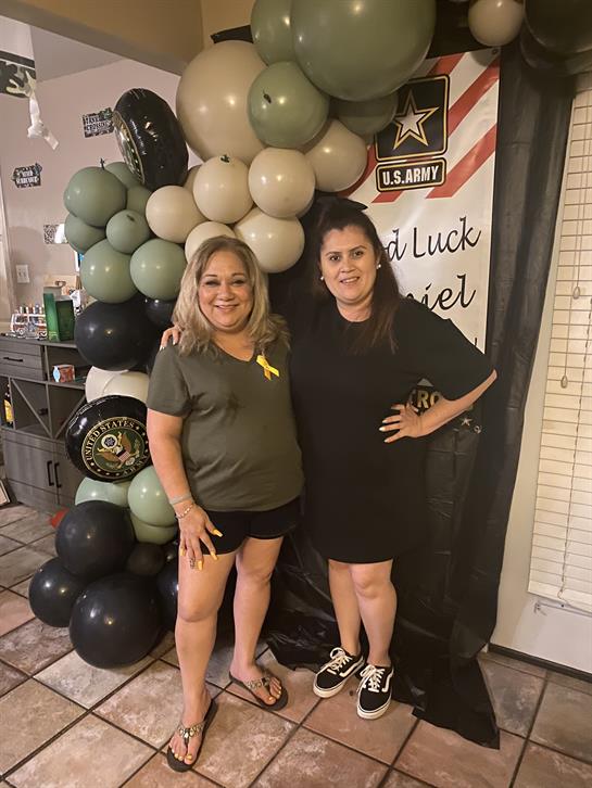 Two friends pose happily together in front of a colorful balloon arch during a farewell party.