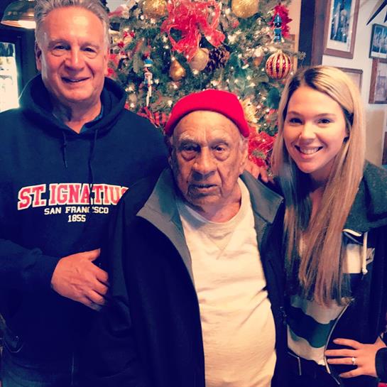 Three family members celebrate together in front of a festive Christmas tree at home.