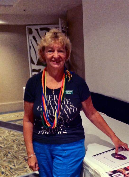 A cheerful woman wearing a rainbow necklace and casual attire engages with others at an event.