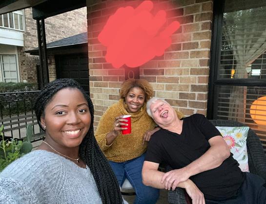 Three friends gather on a patio, enjoying drinks and each other's company while smiling.