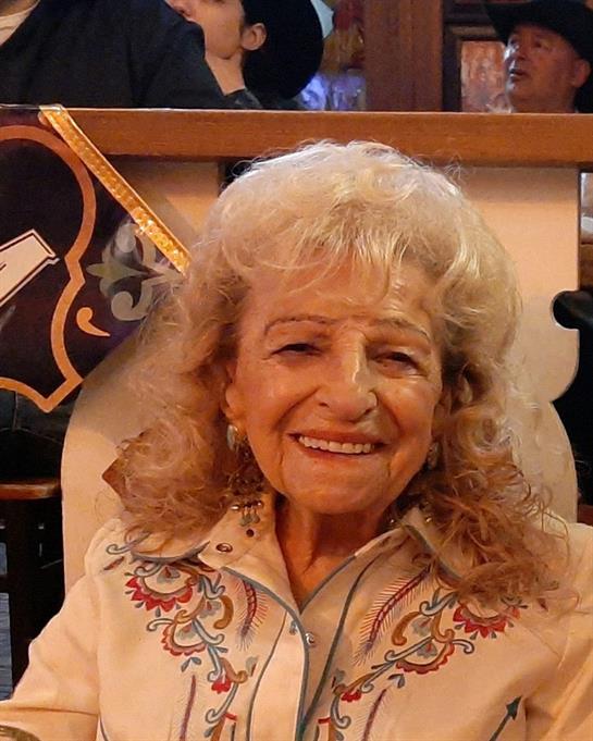 Elderly woman with curly hair smiles warmly while dining at a charming restaurant.