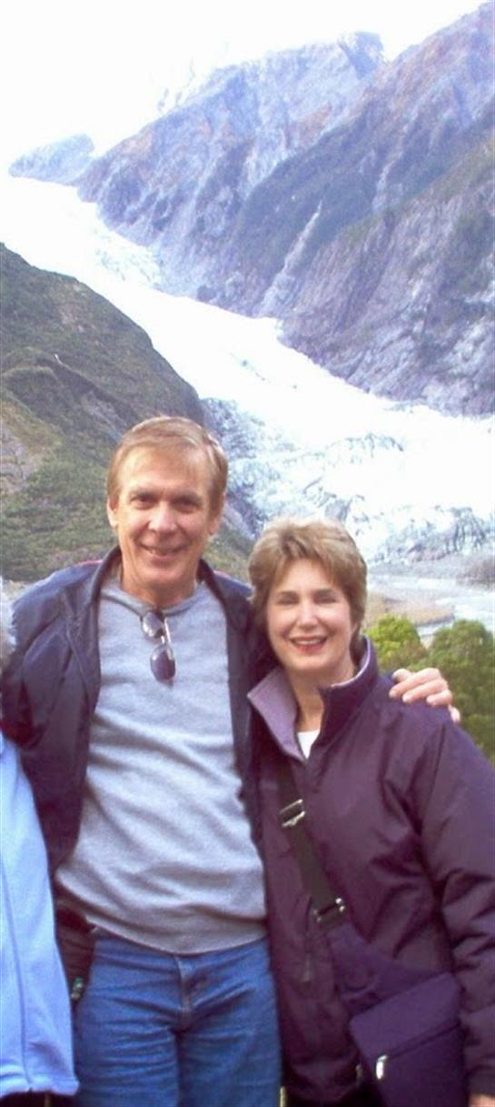 A couple smiles joyfully while posing in front of a glacier in New Zealand's stunning landscape.
