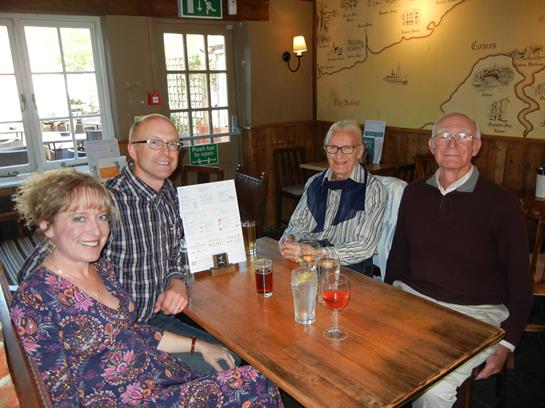 Friends enjoy drinks and laughter at a pub table in the warm afternoon light.