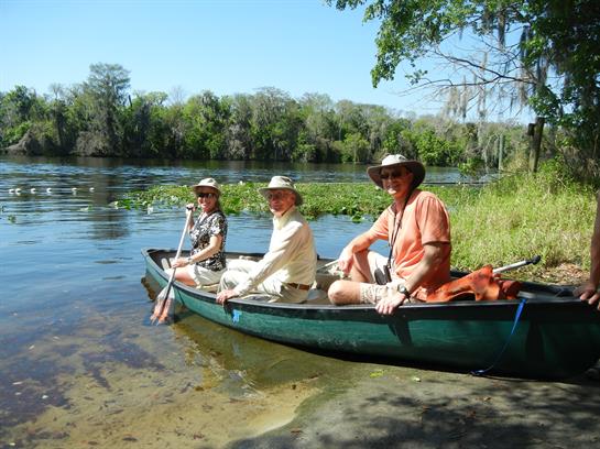 Friends paddle together on a calm river, enjoying nature under the bright blue sky.
