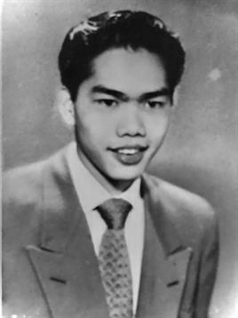 A young man in a suit smiles warmly at the camera in a classic portrait style.
